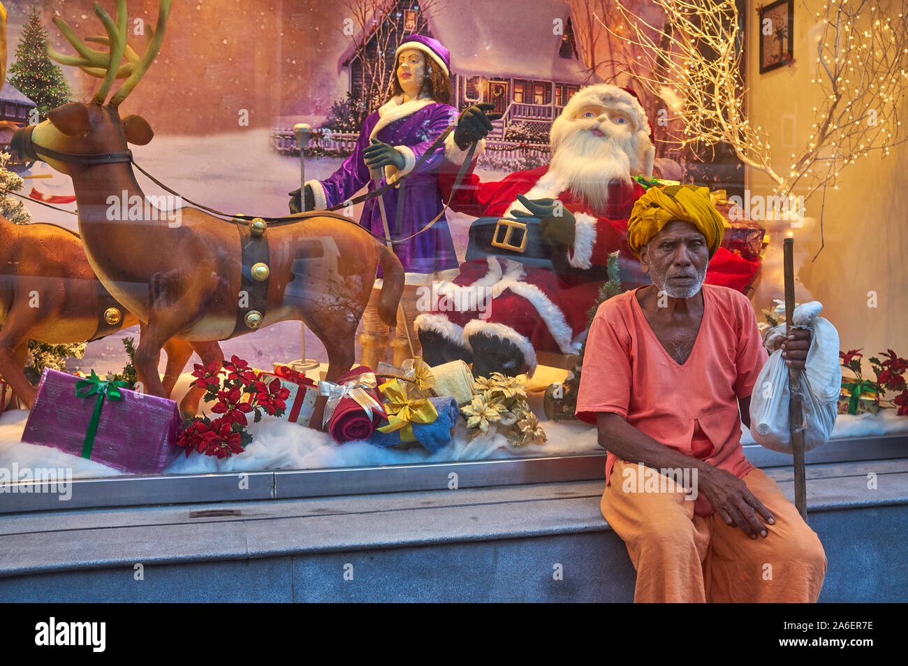 Un turbanned uomo anziano, apparentemente dalla campagna indiana, si appoggia a un negozio finestra Visualizzazione di decorazione di Natale; Colaba, Mumbai, India Foto Stock