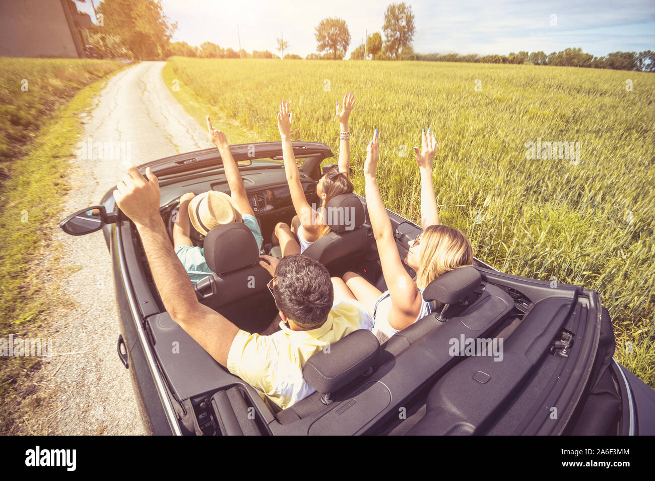Gruppo di amici divertendosi al viaggio in auto. Quattro persone caucasica su una vettura sportiva con in alto le mani. Foto Stock
