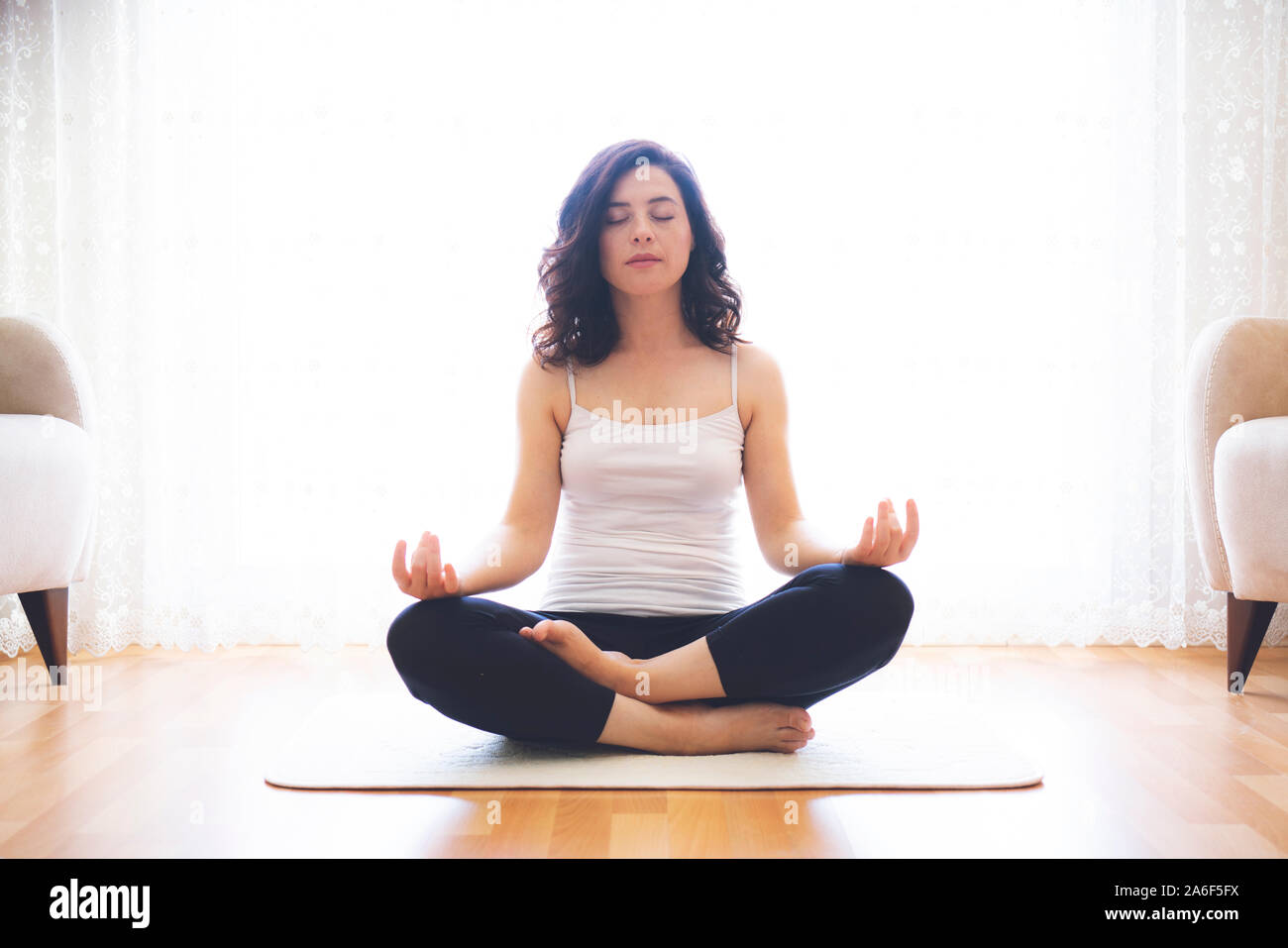 Lo Yoga a casa. Mantenere la calma. Attraente giovane donna seduta sulla posizione del loto sul pavimento con gli occhi chiusi. Foto Stock