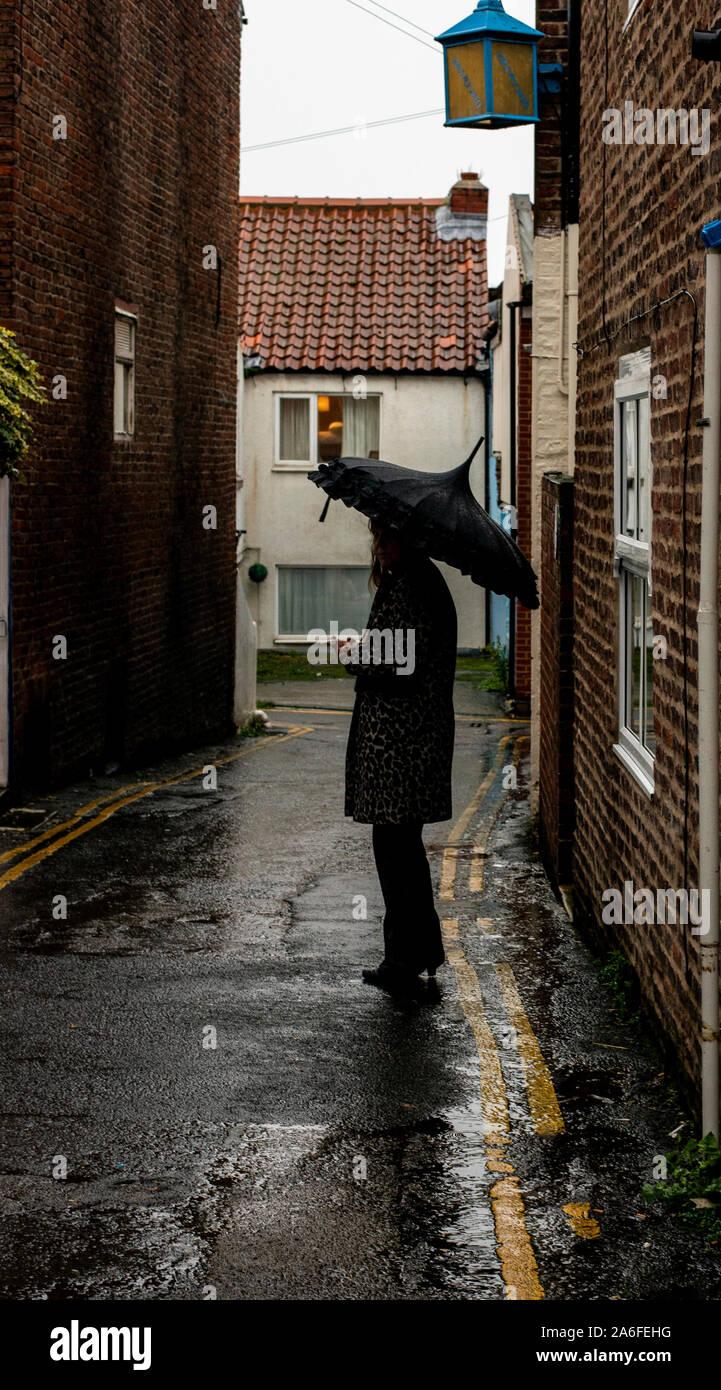 Silhouette di donna in piedi nella pioggia sotto ombrellone, Whitby Goth Festival Weekend, Whitby, North Yorkshire, Regno Unito, 26 Ottobre 2019 Foto Stock