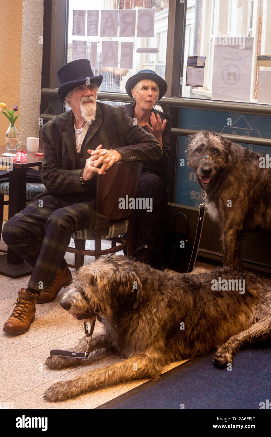 Matura nei tradizionali costumi di Goth con Irish Wolfhound cani in cafe, Whitby Goth Festival Weekend, Whitby, North Yorkshire, Regno Unito, 26 Ottobre 2019 Foto Stock