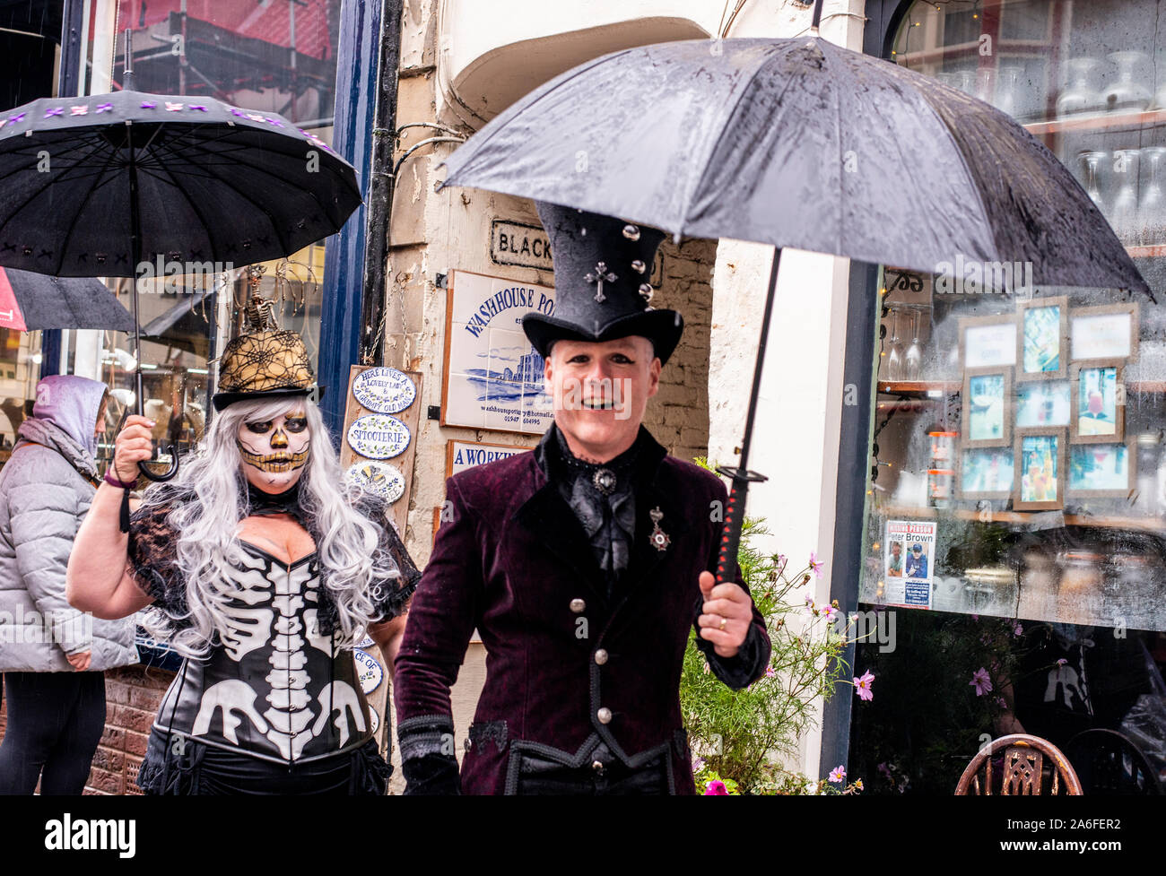 Jolly giovane nei tradizionali costumi di Goth camminando sotto la pioggia, Whitby Goth Festival Weekend, Whitby, North Yorkshire, Regno Unito, 26 Ottobre 2019 Foto Stock
