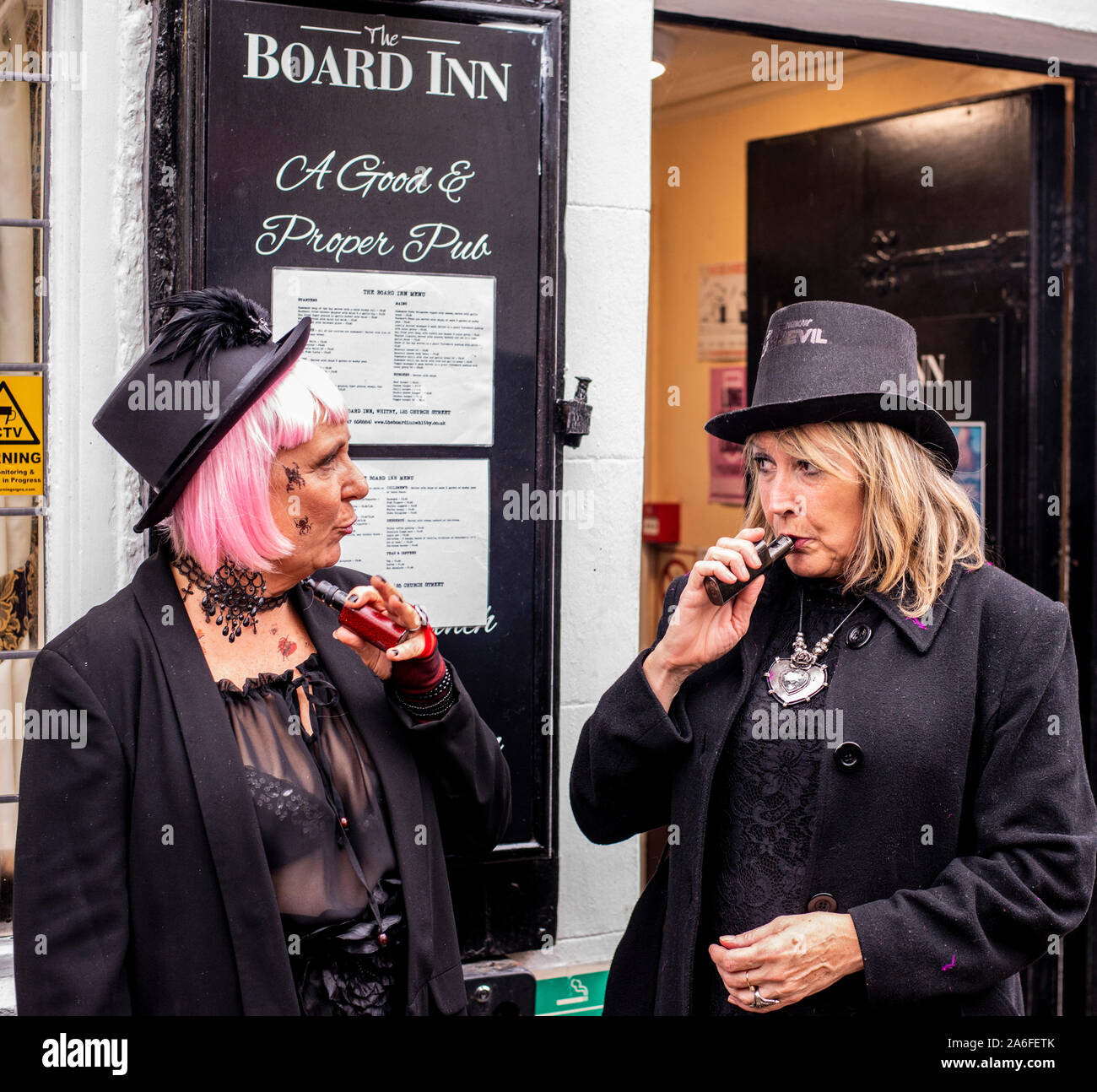 Due donne nei tradizionali costumi di Goth vaping al di fuori di un pub, Whitby Goth Festival Weekend, Whitby, North Yorkshire, Regno Unito, 26 Ottobre 2019 Foto Stock