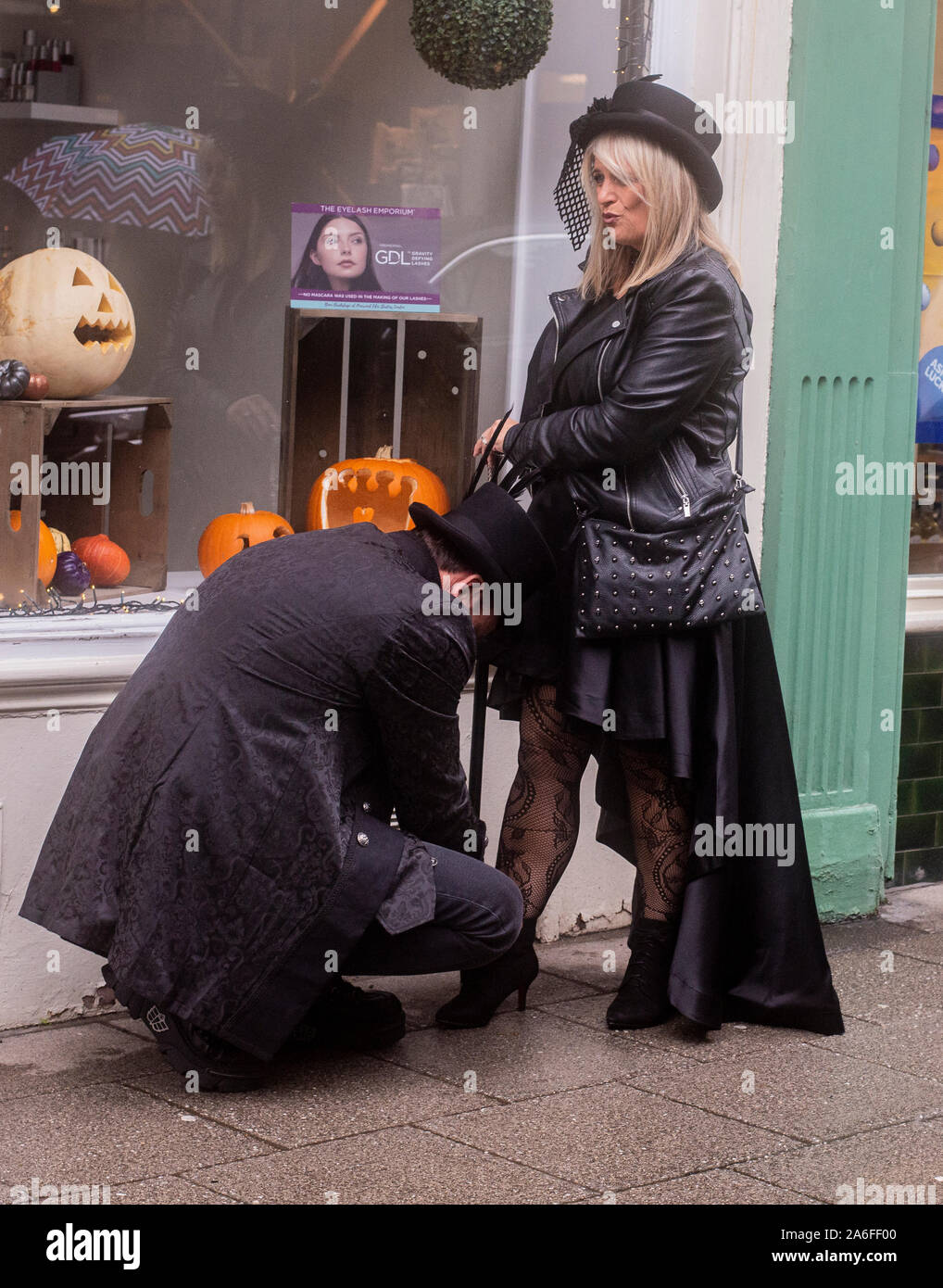 Matura nei tradizionali costumi di Goth con uomo inginocchiato al tirante di donna, passalacci Whitby Goth Festival Weekend, Whitby, North Yorkshire, Regno Unito, 26 Ottobre 2019 Foto Stock