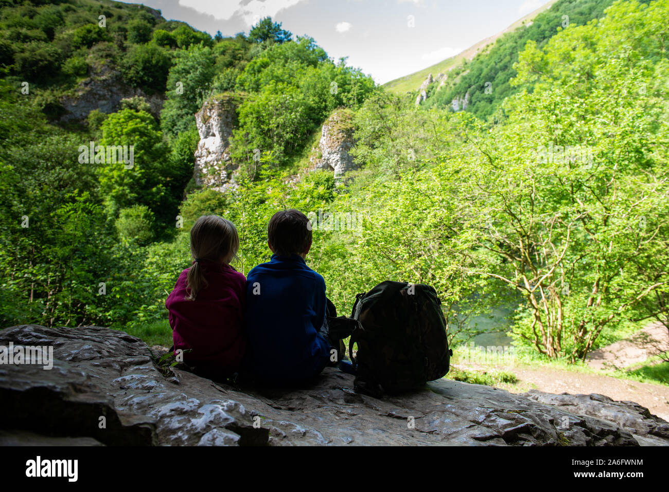 Un ragazzino con ADHD, autismo, Aspergers sindrome, fratello e sorella di seduta in una grotta in alta montagna ammirando e tenendo in vista mentre ri Foto Stock