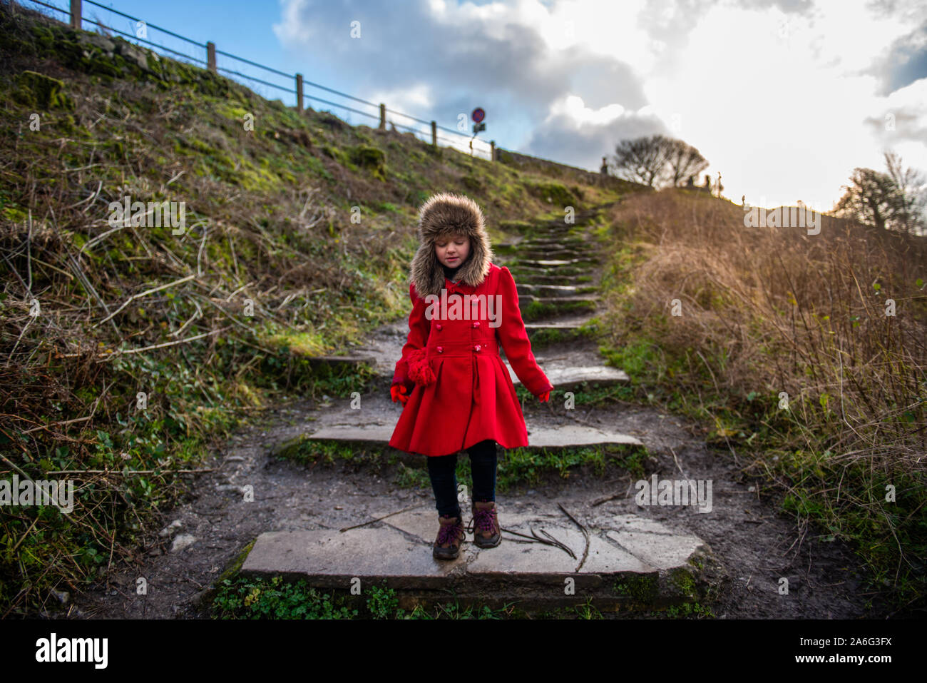 Una graziosa bambina avvolto a caldo in uno spesso rivestimento rosso percorrendo a piedi le fasi a Bakewell viadotto su una fredda mattina, Derbyshire Peak District Foto Stock