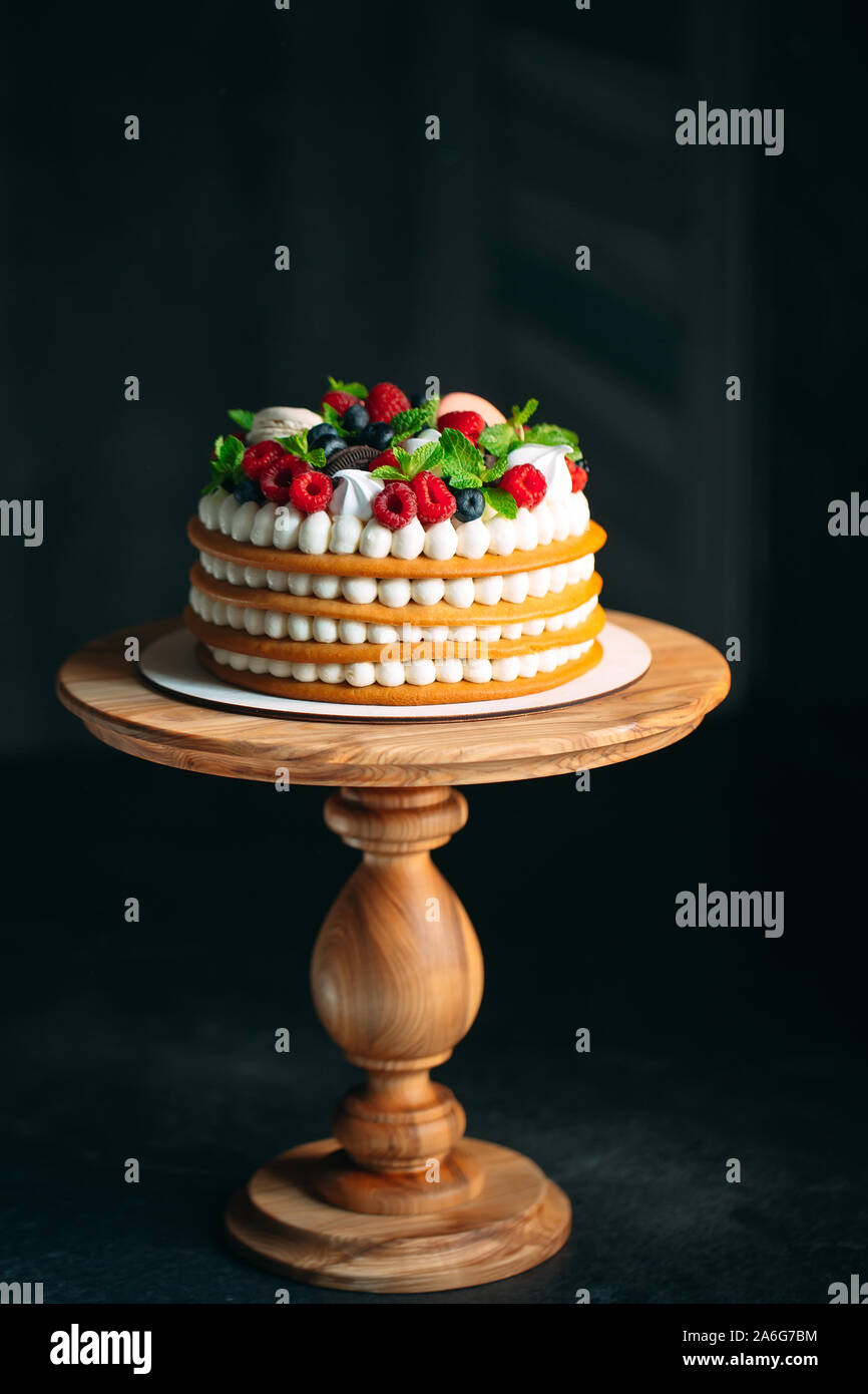 Torta alla frutta. Torta decorata con frutti di bosco su un supporto di legno su uno sfondo nero Foto Stock