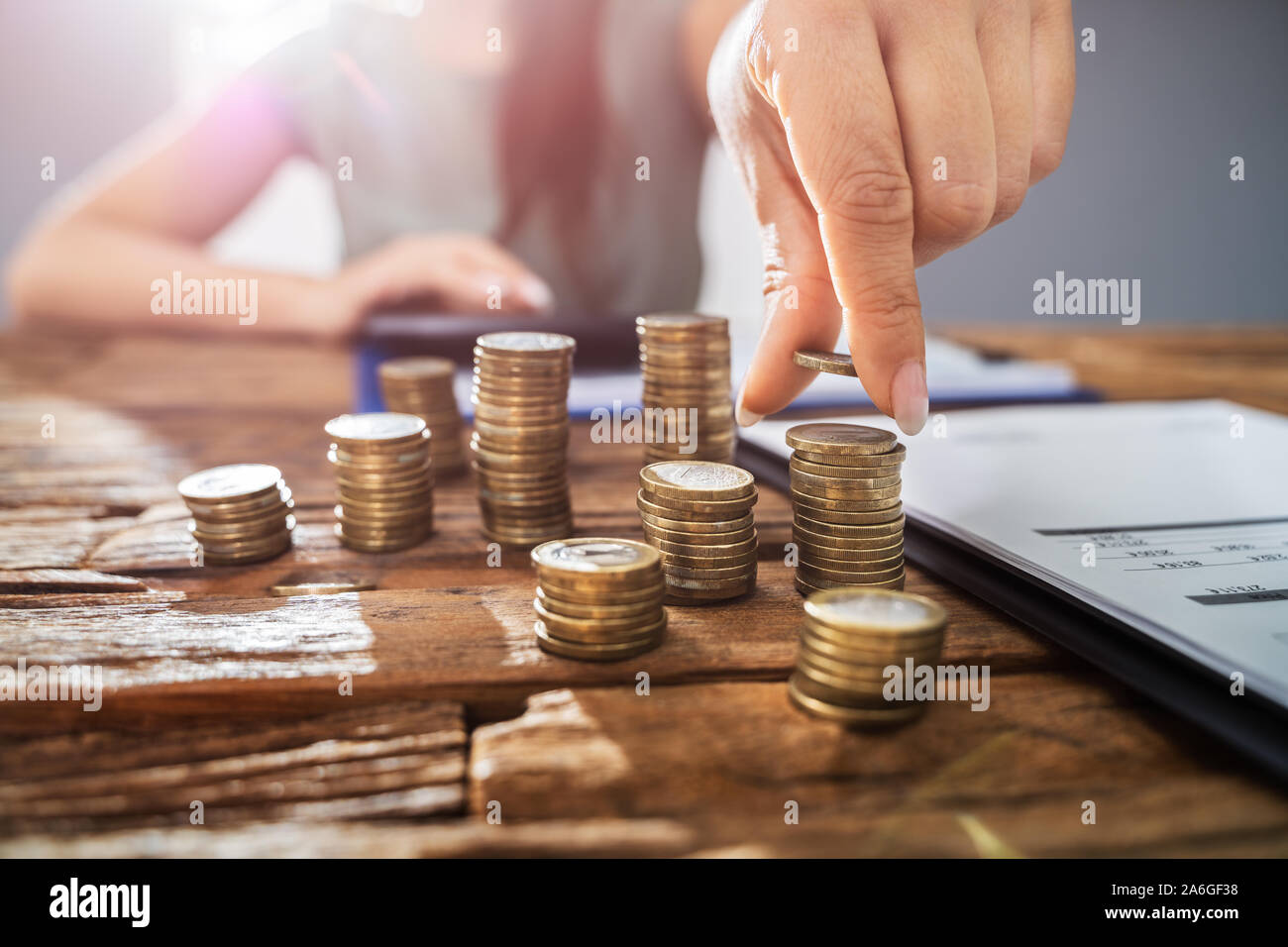 Persona mano facendo il calcolo su monete impilate a scrivania in legno. Le imposte sul reddito concetto Foto Stock