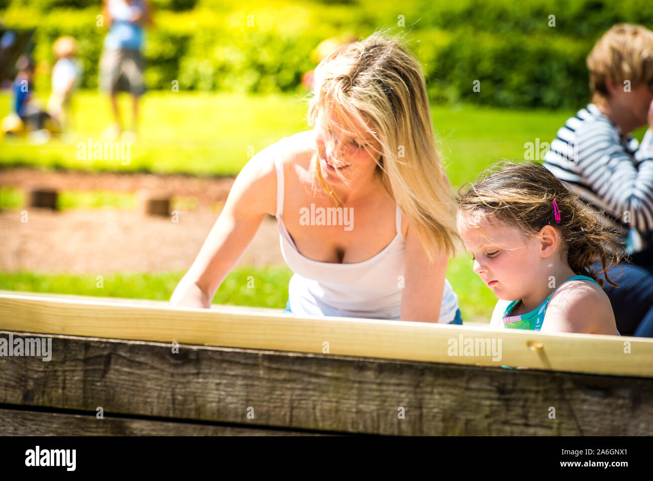 Una bella madre nel 40's coccole giocando con la figlia al parco, giocando con castelli di sabbia, spingendo la sua sulle altalene, Trentham Gardens Foto Stock