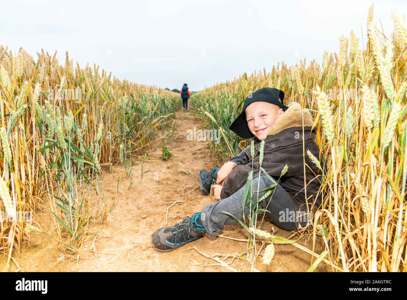 Un cheeky poco ragazzo seduto in un cornfield indossando un cappello da baseball, mentre fuori a giocare con gli amici Foto Stock