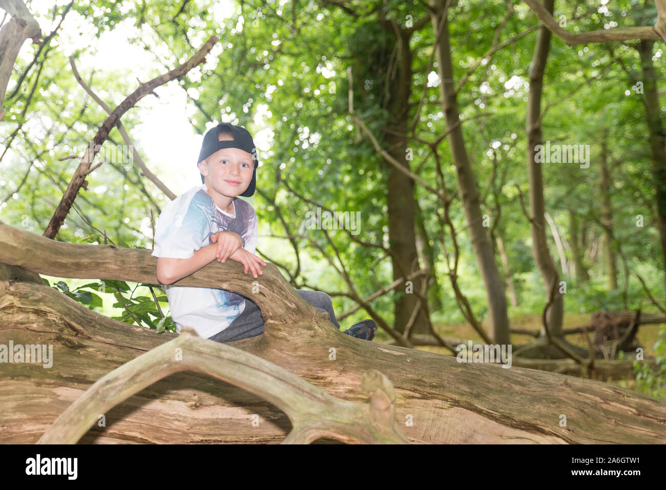 Un cheeky poco ragazzo seduto in un cornfield indossando un cappello da baseball, mentre fuori a giocare con gli amici Foto Stock