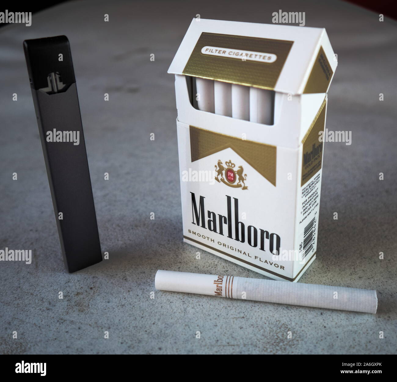 Juul vape pod sigaretta elettronica dispositivo con un pacchetto di sigarette Marlboro e una sigaretta collocato al di fuori su di un bianco tavola testurizzato, isolato Foto Stock