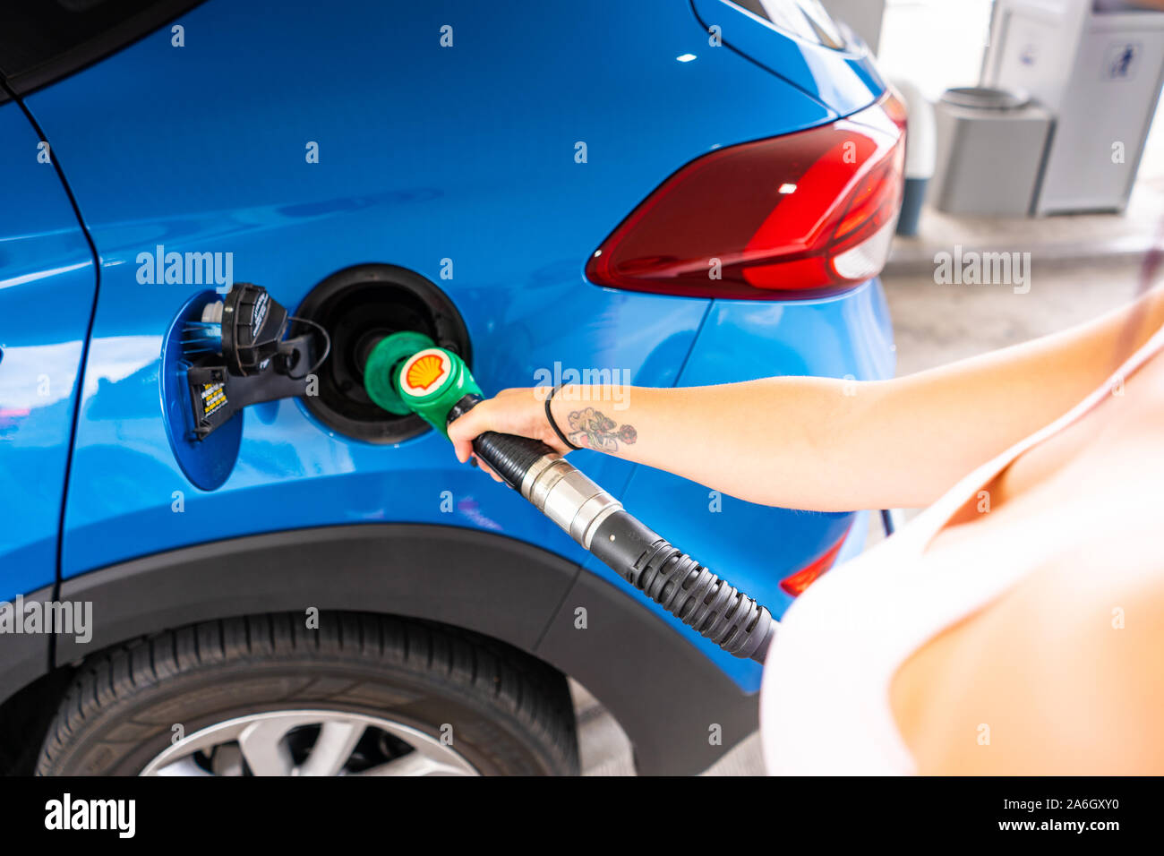 Un giovane slim donne con capelli viola si riempie la sua auto con benzina senza piombo, il distributore di benzina Shell Foto Stock