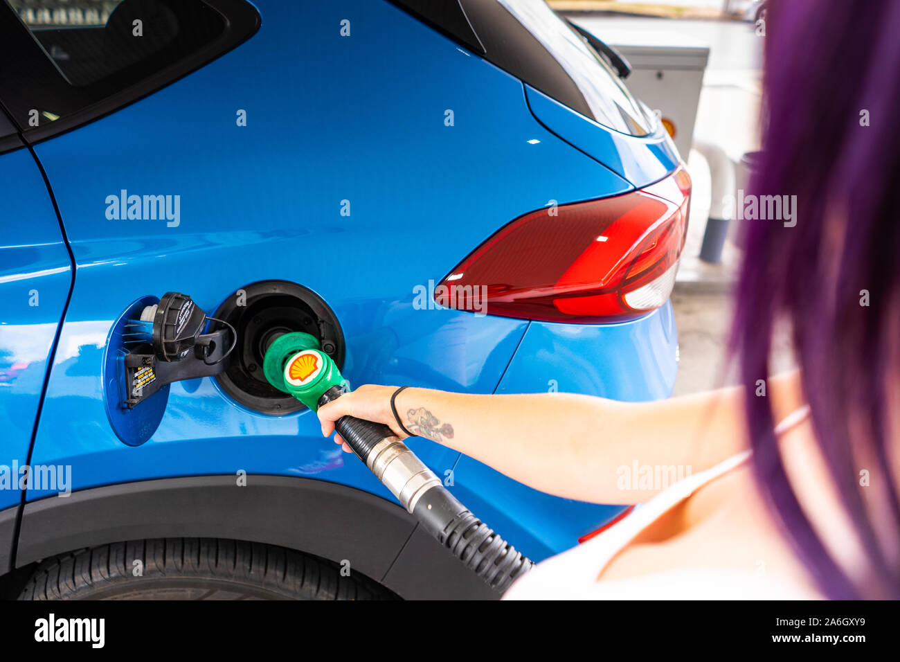 Un giovane slim donne con capelli viola si riempie la sua auto con benzina senza piombo, il distributore di benzina Shell Foto Stock