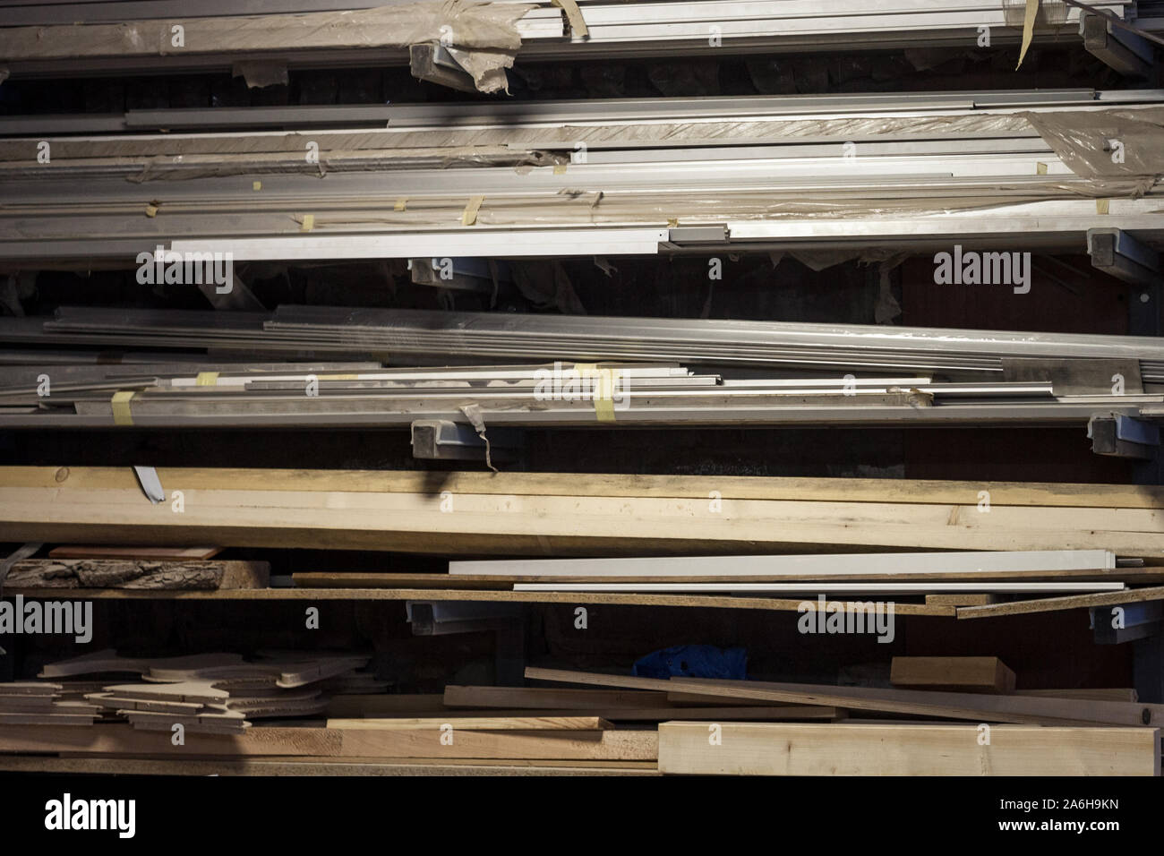 Aste metalliche e gli alberi in alluminio così come tavole di legno e travi di legno store allentati sugli scaffali di un falegname workshop immagine della st Foto Stock