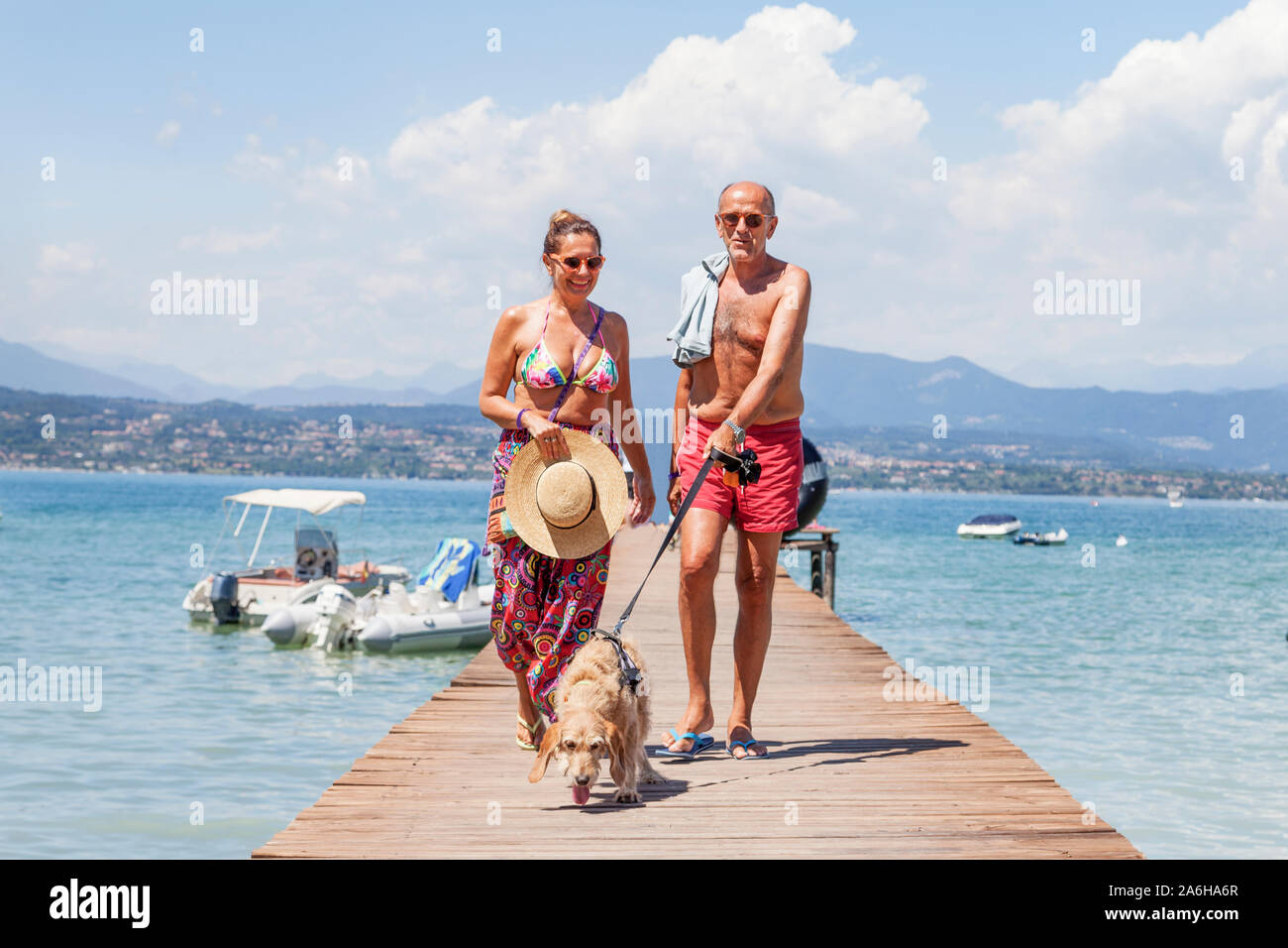 Coppia matura rilassante in costume da bagno a piedi con un cane sul dock di un resort. Concetto di bella gente divertirsi in estate Foto Stock