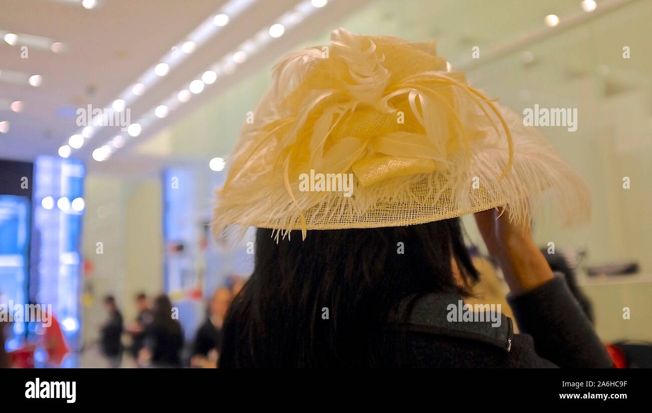 Retro della testa di donna indossando grande giallo pastello canestro con cappello di piume, all'interno luminoso spazio pubblico Foto Stock