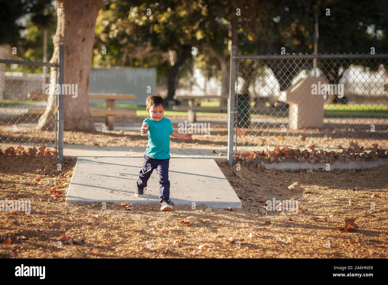 Un ragazzino corre veloce in un parco giochi con gating durante la stagione autunnale. Foto Stock