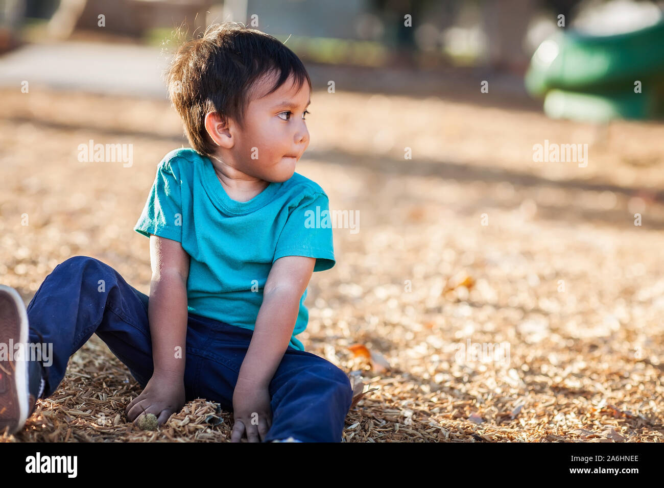 Latino ragazzo con le mani sporche di giocare con woodchips da un parco giochi tutti da lui stesso e guardando lontano. Foto Stock