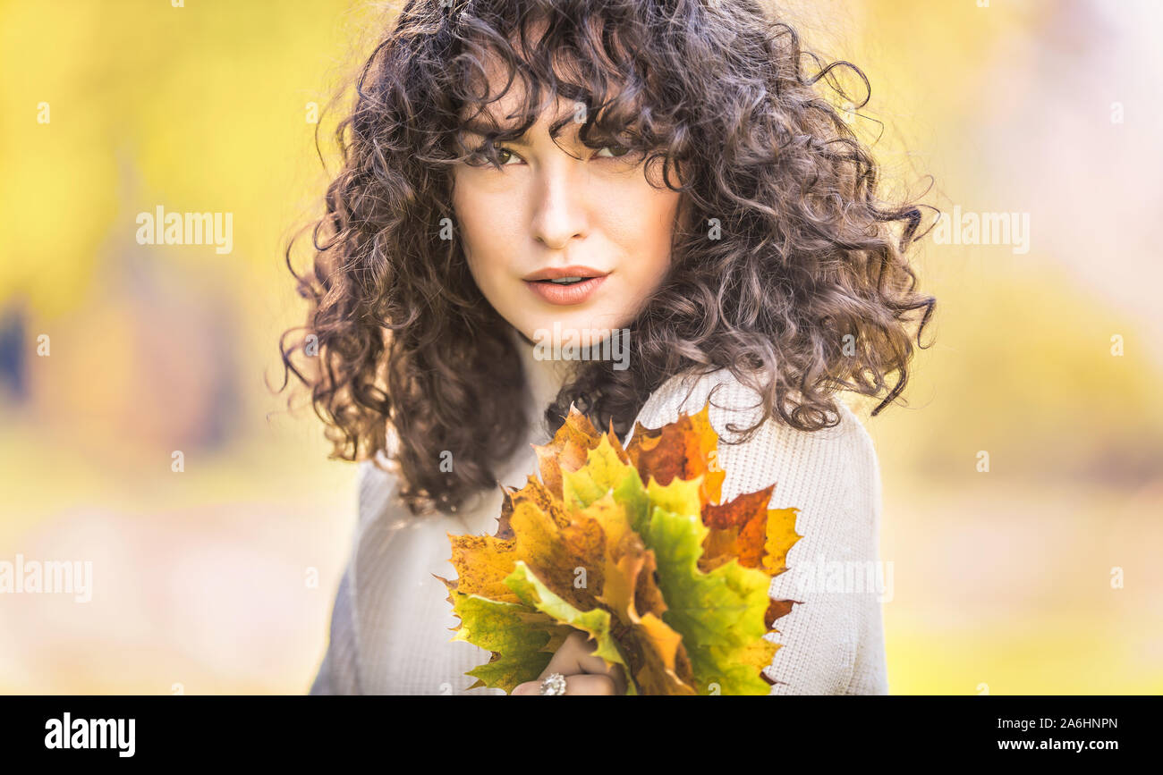 Autunno Ritratto di giovane donna con i capelli ricci e bouquet di foglie di acero. Foto Stock