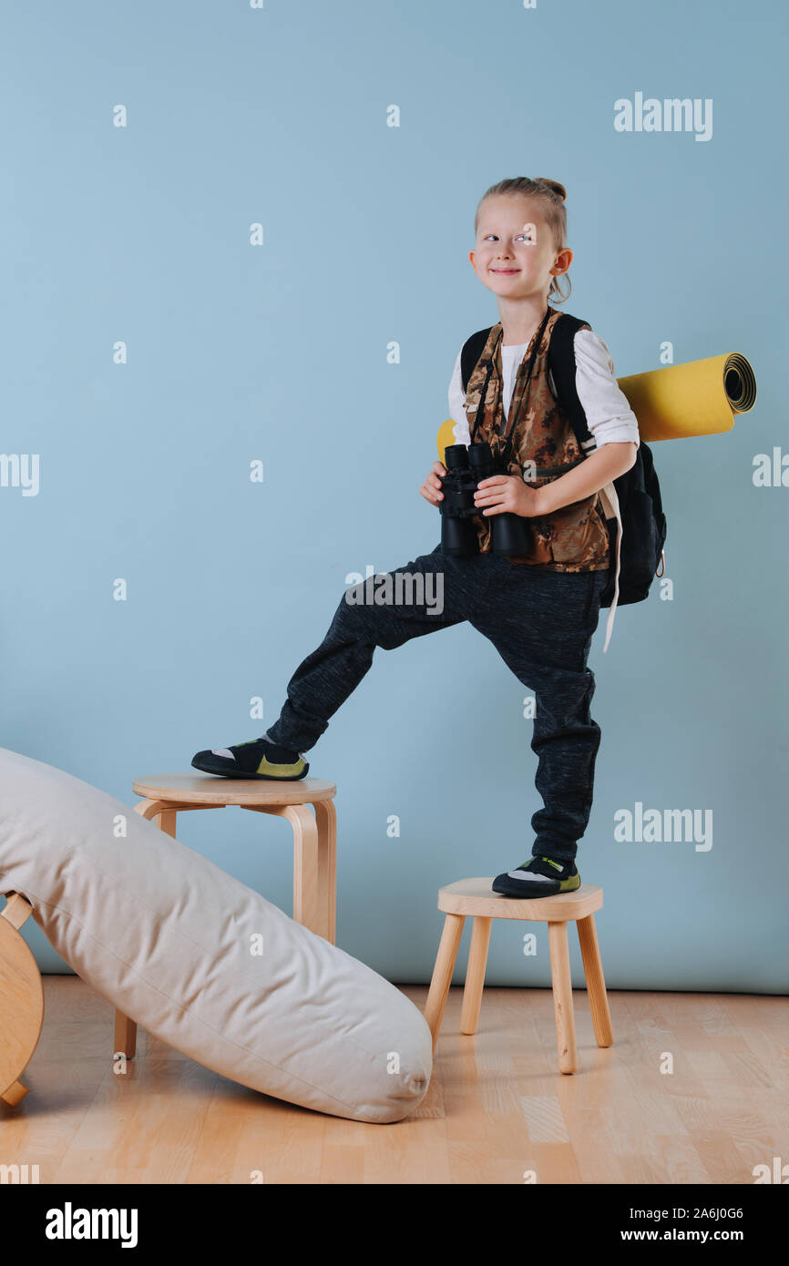 Ritratto di un ragazzino con il binocolo climbing sgabelli, riproduzione di un escursionista a casa Foto Stock