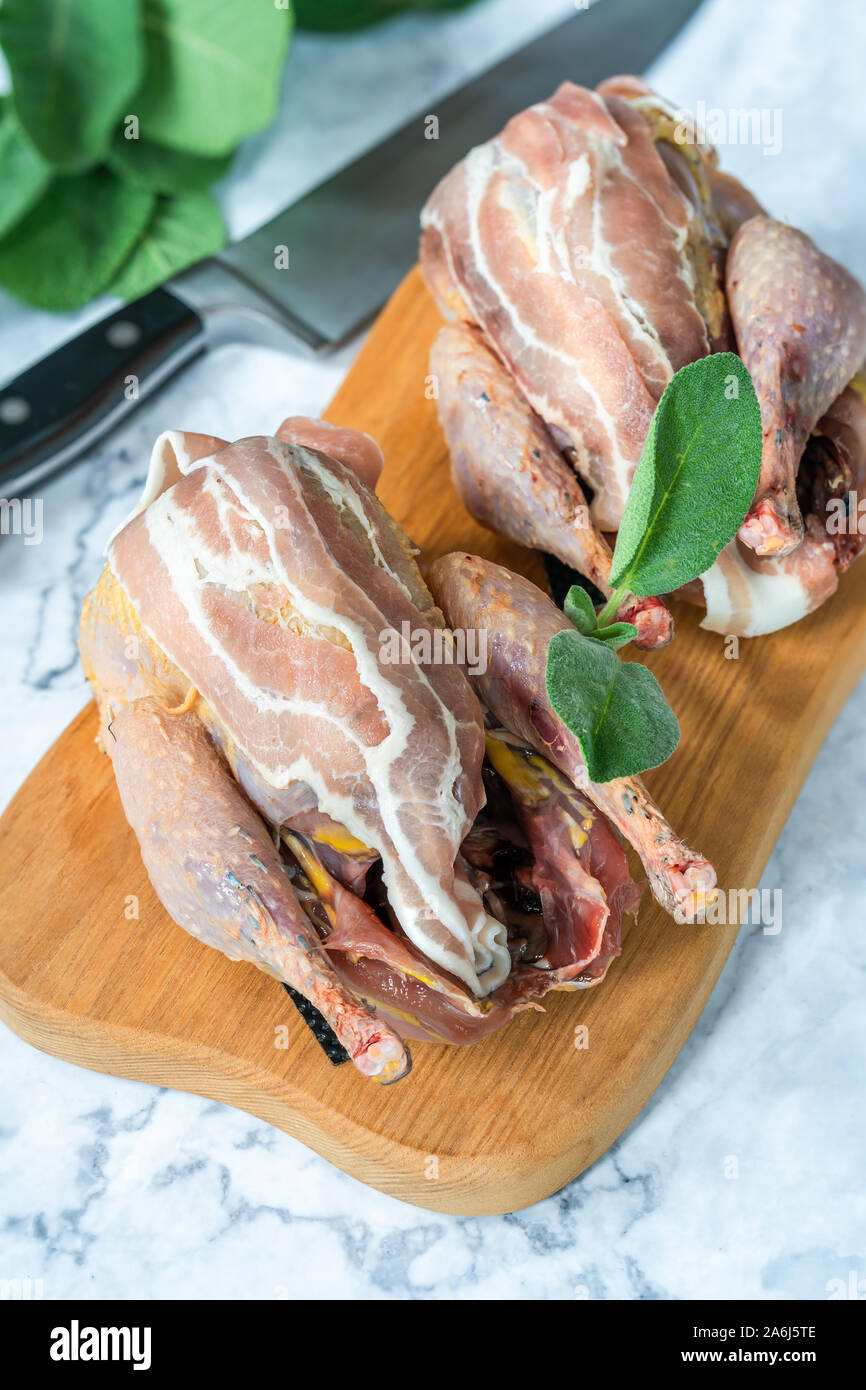 Due nuove materie fagiani avvolto in pancetta preparato per la cottura sul pannello di legno Foto Stock