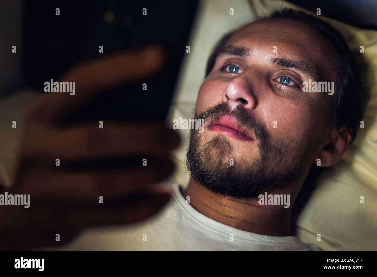 Giovani belli e stanchi con barba non riesce a dormire e guardare qualcosa sul suo telefono cellulare di notte. Foto Stock