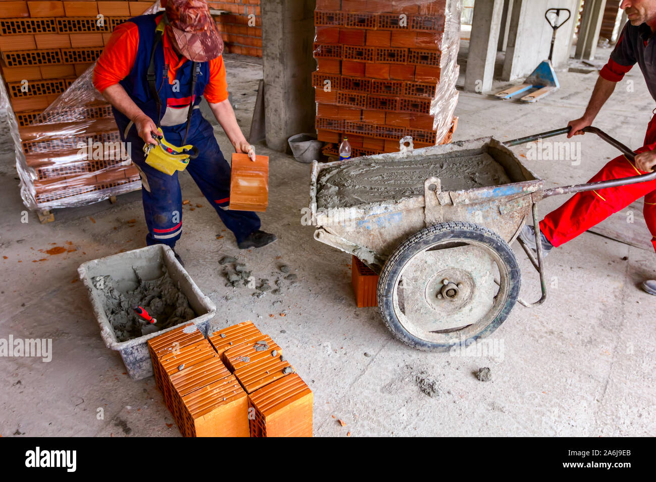 Lavoratori edili sono utilizzando le loro risorse umane per gestire carriola con mortaio fresco al sito in costruzione. Foto Stock