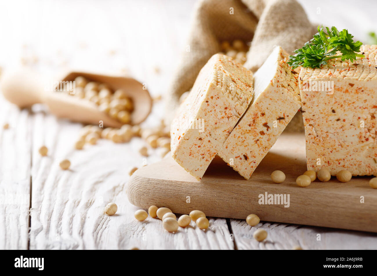 Fagiolo di soia tofu cagliata sul tagliere e nel sacco di canapa su bianco cucina in legno tavolo. Non a base di latte sostituto alternativo per formaggio Foto Stock