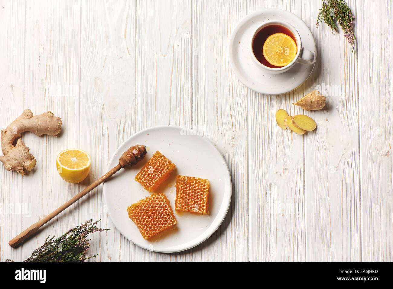 Piatto di laici favi con cucchiaio di miele, limone, lo zenzero e la tazza di tè su un bianco sullo sfondo di legno. Medicina Naturale concetto. Foto Stock