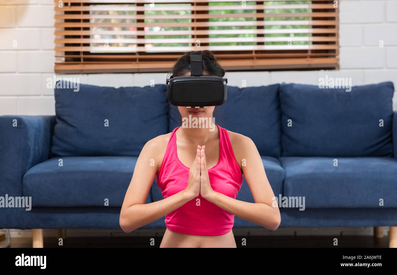 Giovane donna asiatica in realtà virtuale bicchieri fa Yoga e Aerobica a casa,futuro concetto tecnologico. Foto Stock