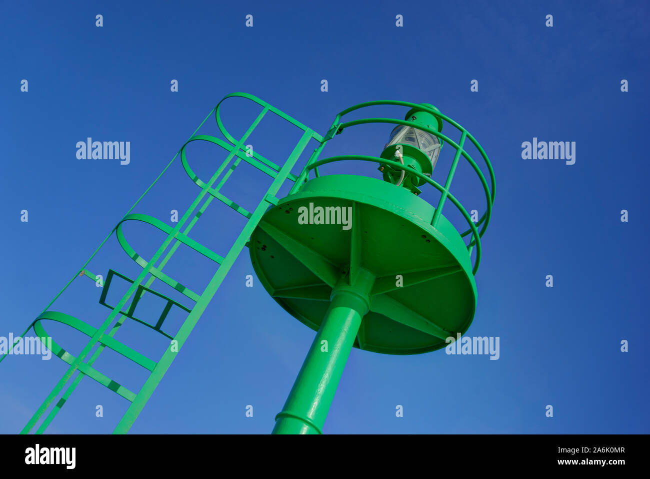 Top of large land based green navigation buoy with access ladder against bright blue sky Foto Stock