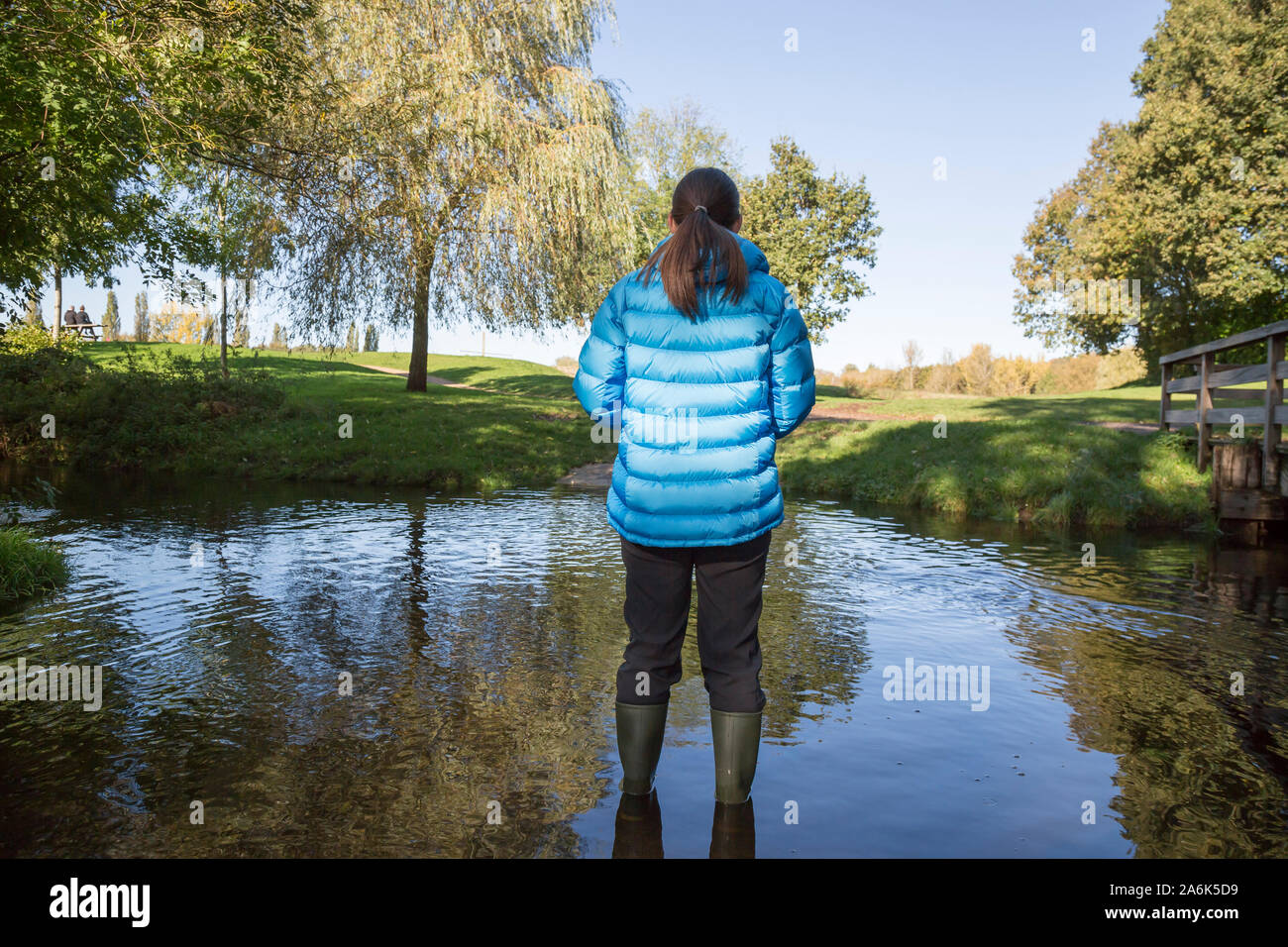 Dopo la pioggia: vista posteriore di una femmina (indossando wellies) isolato all'aperto nell'autunno del sole in piedi in acqua dopo giorni di pioggia continua nel Regno Unito. Foto Stock