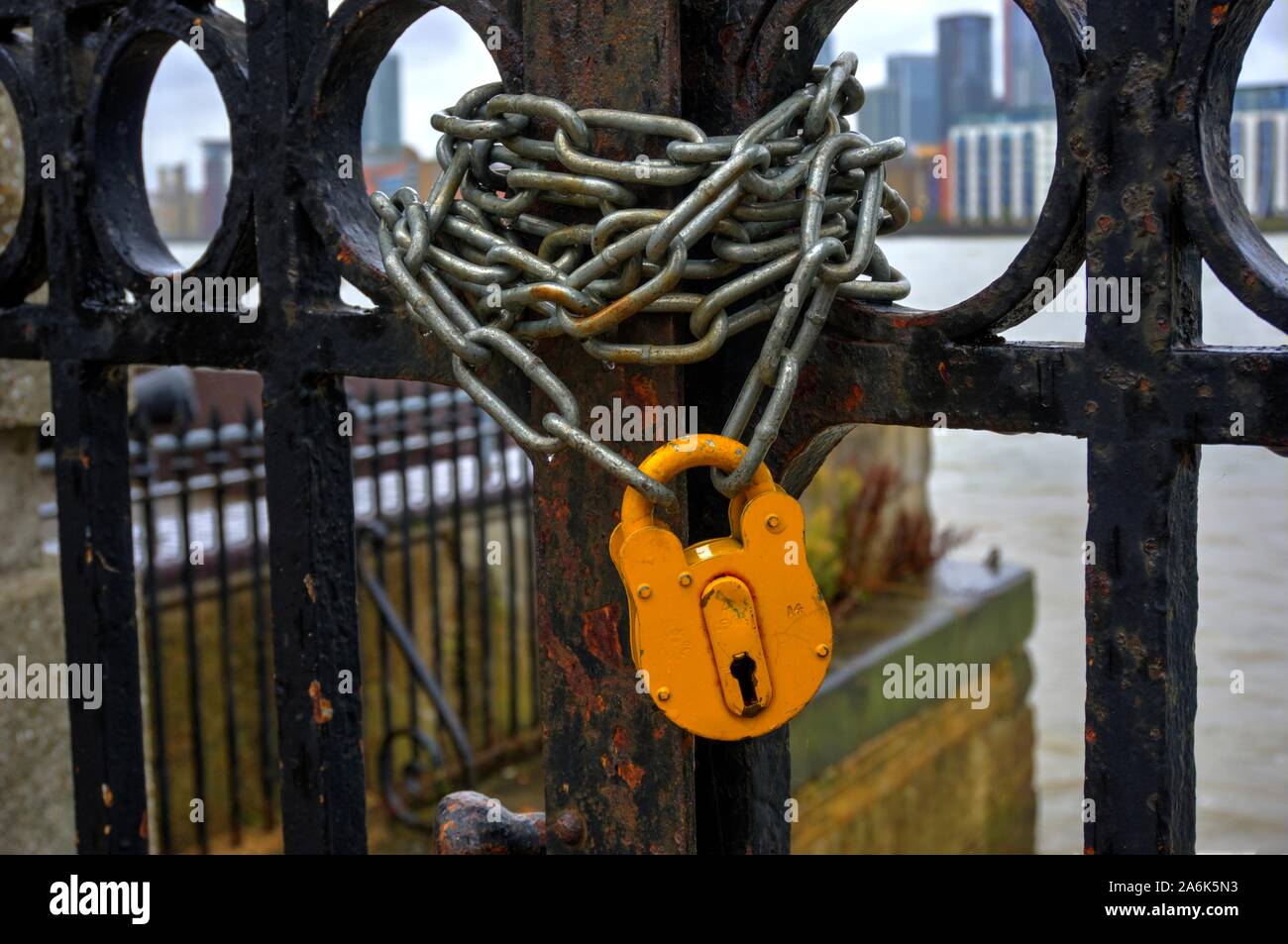 Lucchetto giallo e la catena sulla cancellata in ferro battuto che conduce al fiume Foto Stock