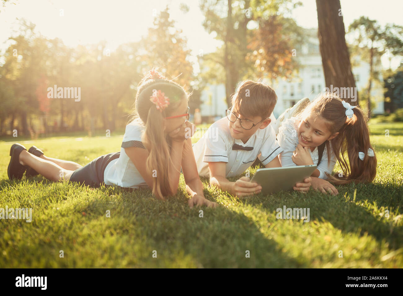 Tre sorridente in età scolastica sono amici sdraiati sull'erba e guardando il tablet Foto Stock