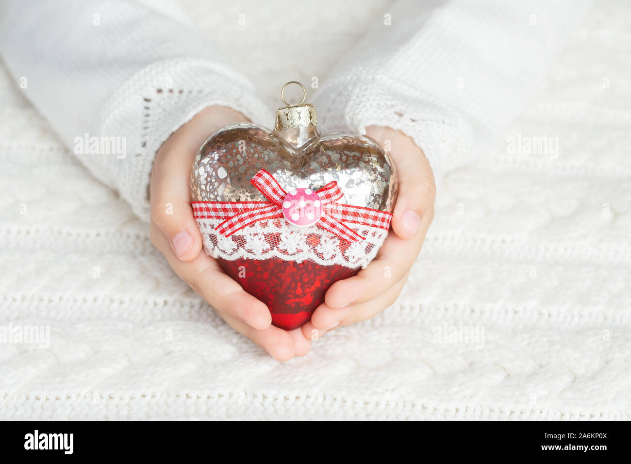 Bambino tiene un cuore di vetro, un giocattolo di Natale nelle mani sullo sfondo di un maglione caldo. Foto Stock