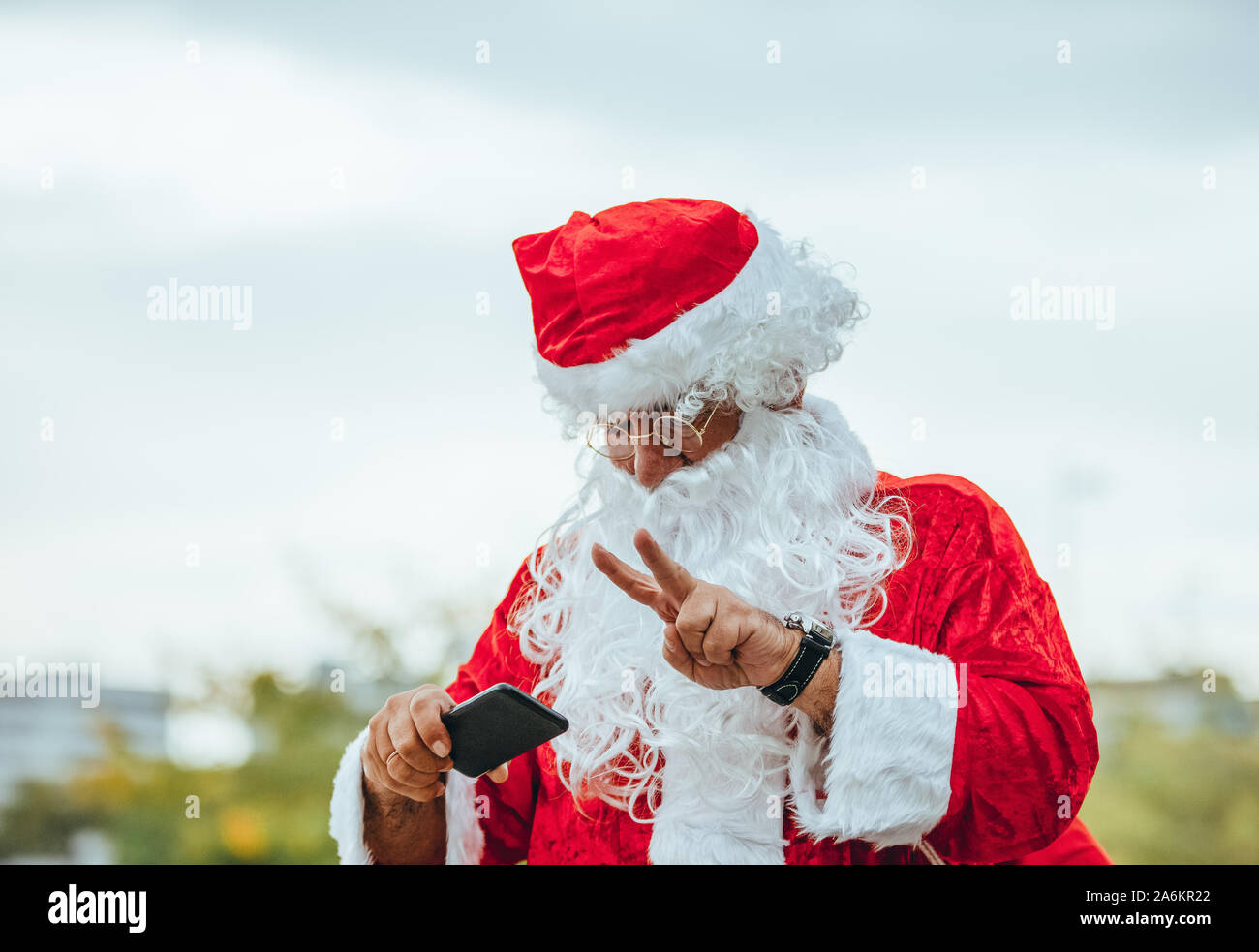 Foto di stock di Santa Claus facendo una selfie con il cellulare in una mano e l'altra rendendo il simbolo della vittoria. Il tempo di Natale Foto Stock