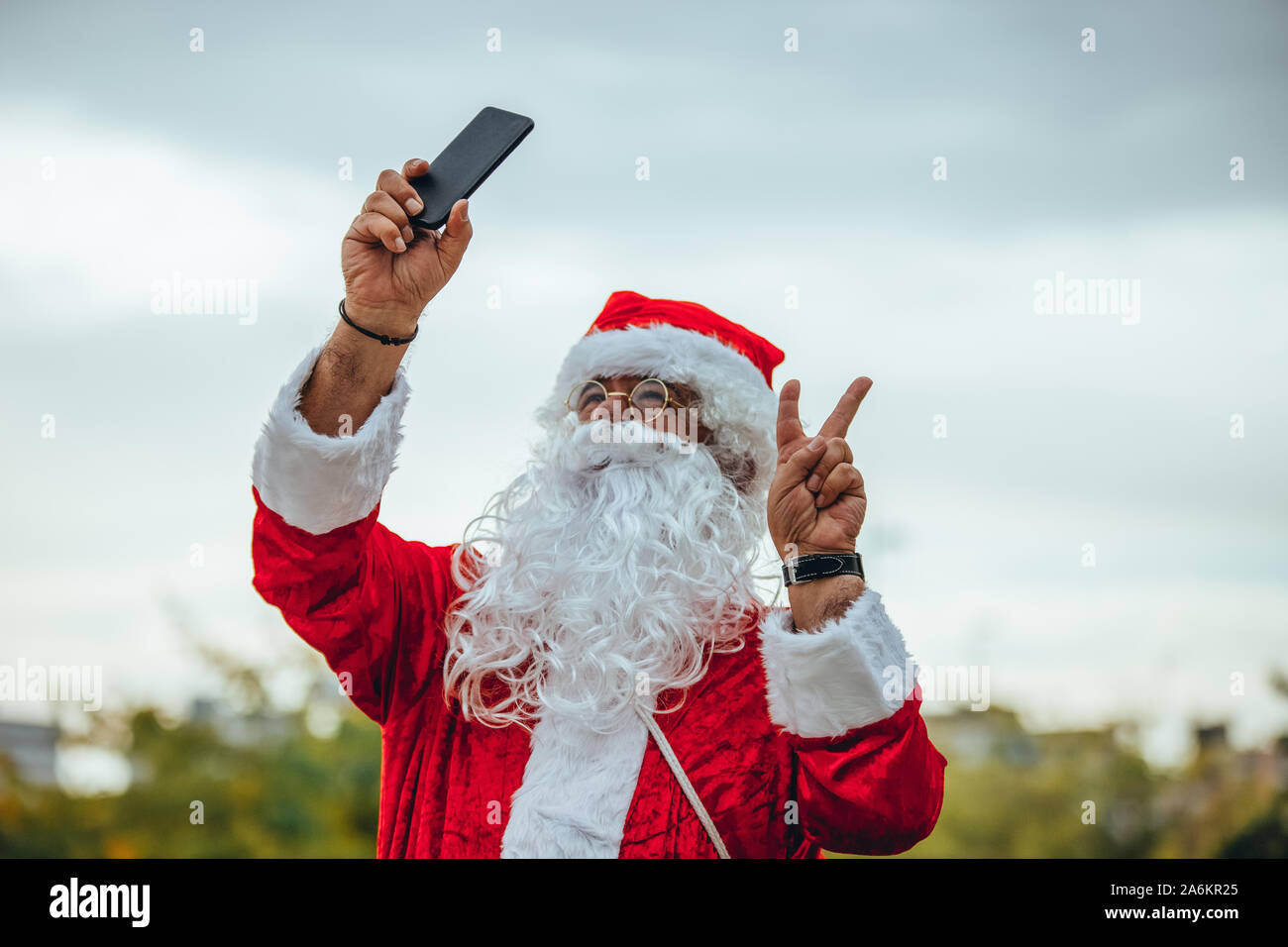 Foto di stock di Santa Claus facendo una selfie con il cellulare in una mano e l'altra rendendo il simbolo della vittoria. Il tempo di Natale Foto Stock
