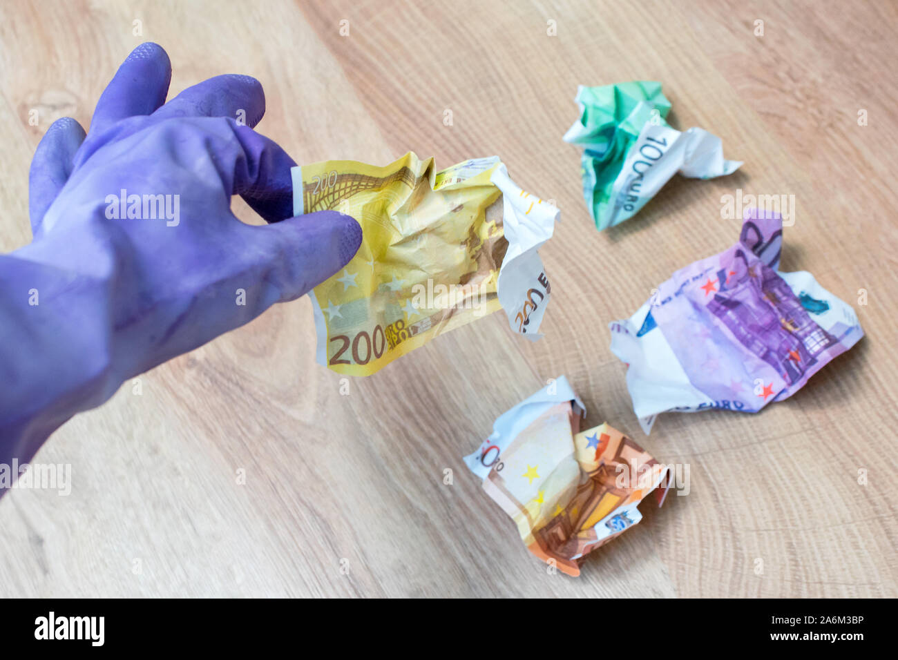 La mano in viola i guanti di gomma per la pulizia azienda accartocciata fatture in euro su un sfondo di legno. Pagamento per lavoro, cestino di denaro, l'inflazione, il tema dei rifiuti. Foto Stock