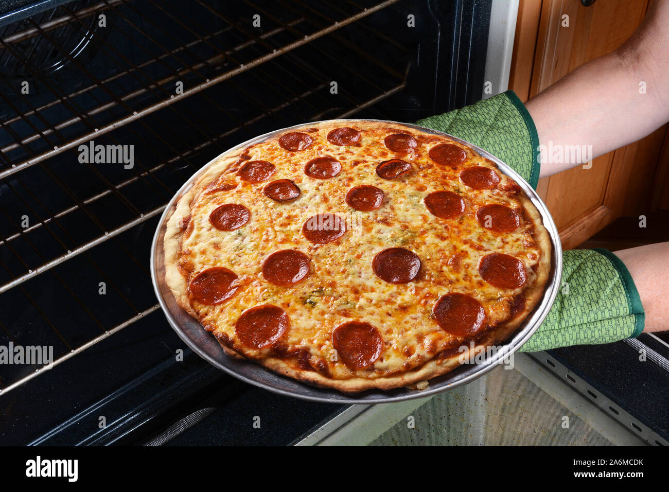 Primo piano di una donna prendendo un fresco pizza cotta al forno la torta dal forno. Orizzontale con womans mani in guanti da forno solo. Foto Stock