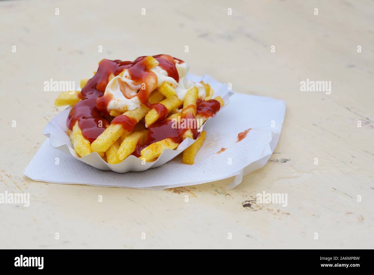 Patate fritte con la maionese e ketchup in un piatto di cartone esterno su un dipinto di tavolo in legno e malsano, fast food, in Germania chiamato pommes w rossa Foto Stock