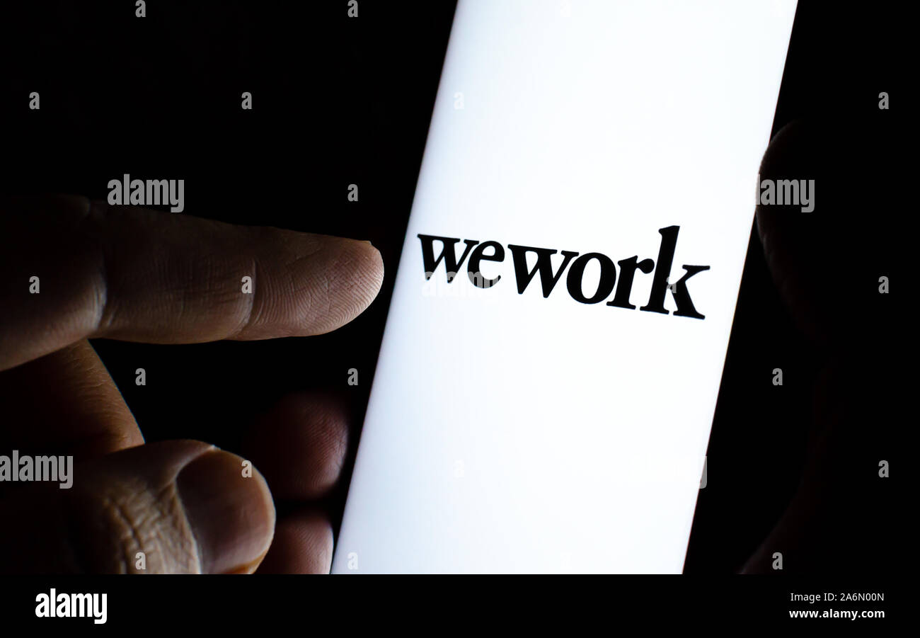 WeWork company logo sullo schermo dello smartphone in una stanza buia e un dito puntato a. WeWork fornisce lo spazio in ufficio e area di lavoro soluzioni. Foto Stock