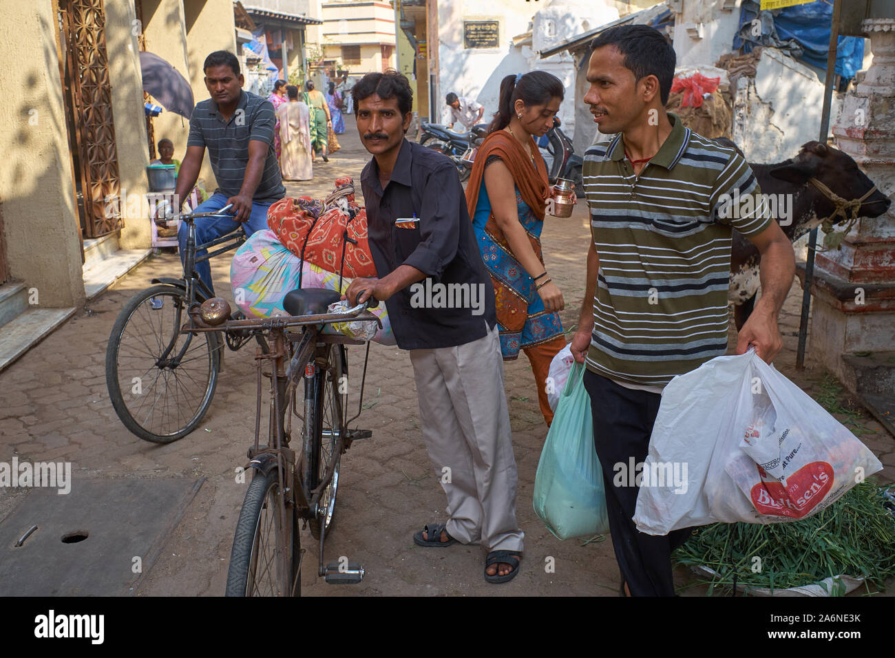 Scena di strada in Mumbai, India, occupato pedoni, ciclisti e una mucca condividere lo spazio stretto in una corsia Foto Stock