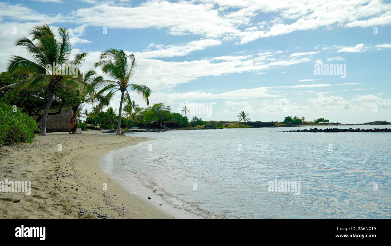 Spiaggia di sabbia bianca di curvatura intorno all Oceano Pacifico costa, circondato da alberi di palma e nuvoloso cielo blu Foto Stock