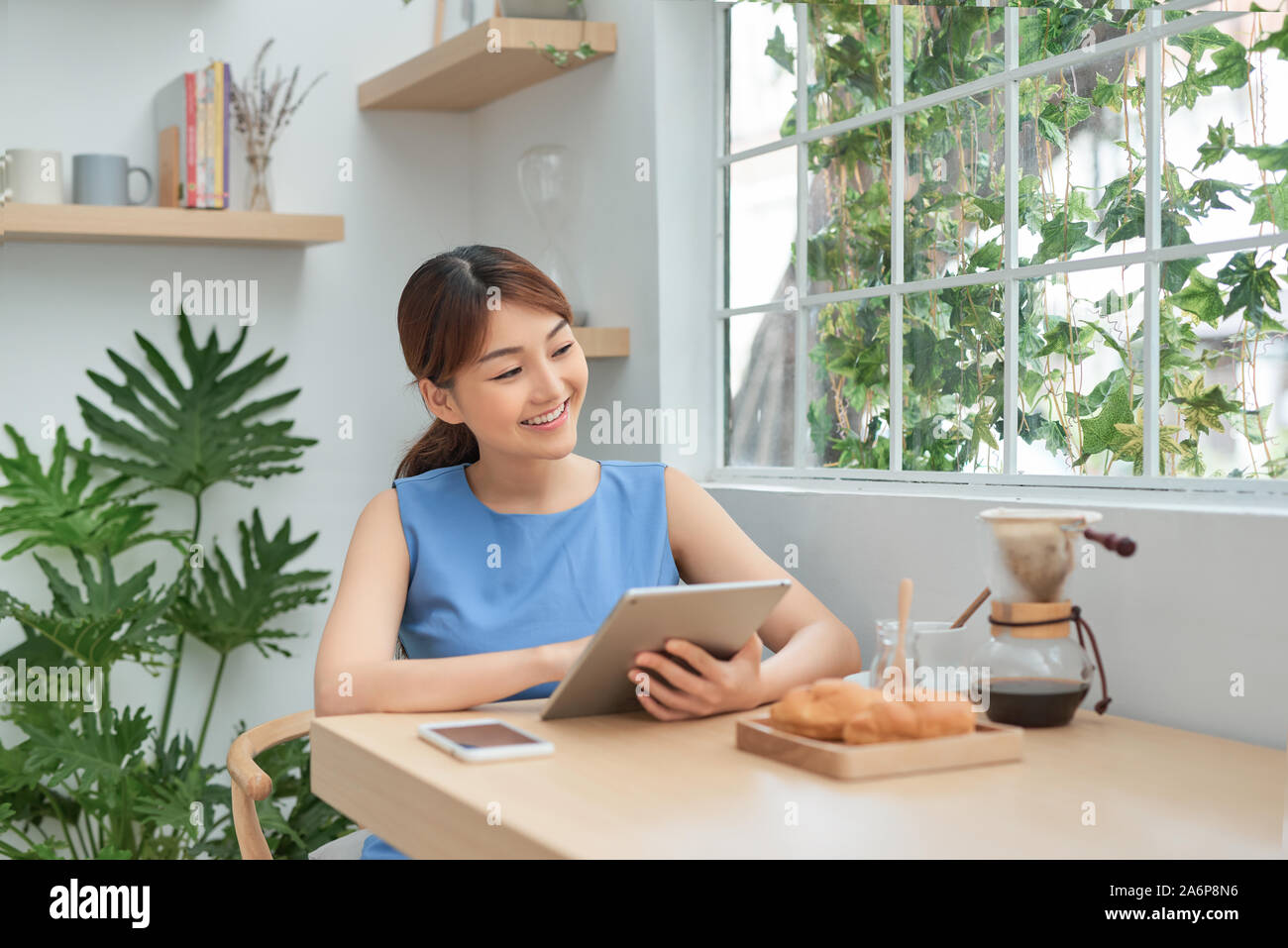 Ritratto di felice giovane ragazza asiatica utilizzando tablet mentre è seduto dietro la finestra di mattina Foto Stock