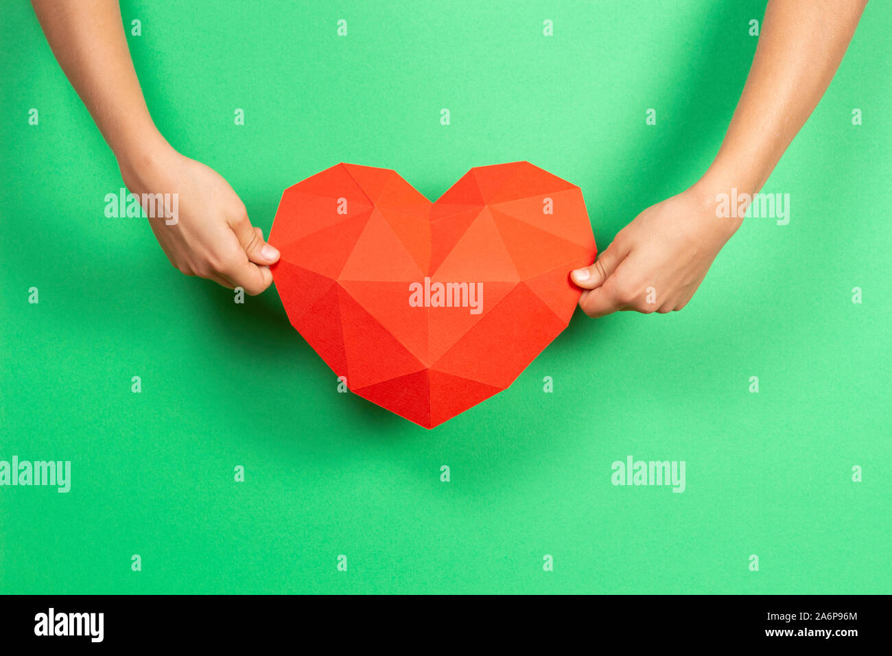 Mani rosso carta poligonale forma di cuore su sfondo verde chiaro Foto Stock