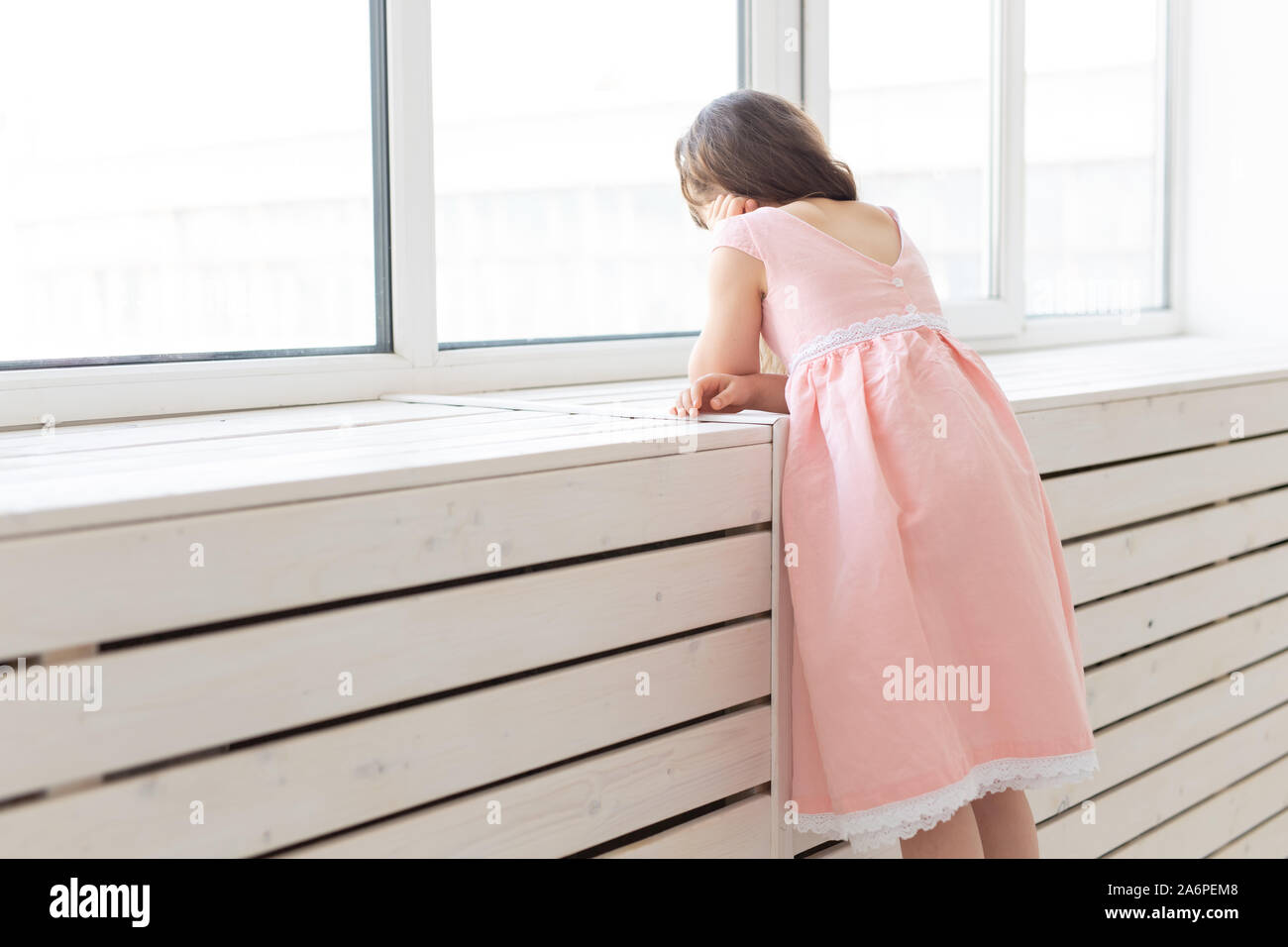 Trasognata piccola ragazza in un abito rosa guarda fuori dalla finestra Foto Stock