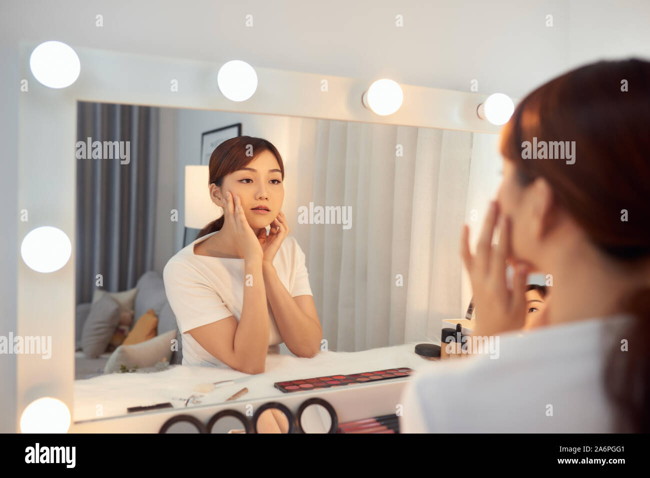Infelice giovane donna asiatica di fronte a uno specchio guardando il suo rughe Foto Stock