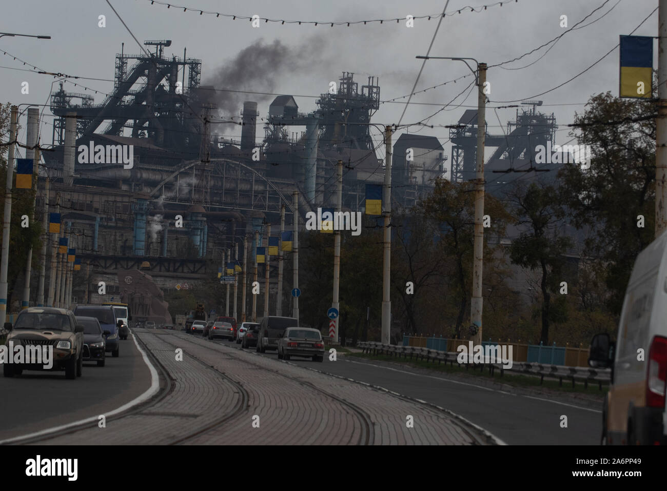 Auto vanno da un Azov Stal impianto siderurgico avenue in Mariupol.I due grandi impianti metallurgici basato in Mariupol sono i Azovstal Ferro e acciaio di opere e la Ilyich Ferro e acciaio opere parte del Gruppo Metinvest. Secondo l ecologia ucraino Ministero relazione nel 2016 Ilyich pianta prodotti più di 1,7 milioni di tonnellate di emissioni nocive in atmosfera e di Azov Stal prodotta 78,600 tonnellate di inquinanti atmosferici e versato 1,4 milioni di metri cubi di rifiuti nel Mar di Azov situate a. Nel 2018 l'Ucraina del Ministero della Sanità ha messo in guardia il pubblico per evitare di nuotare in qualsiasi delle spiagge intorno a Mariupol. Foto Stock