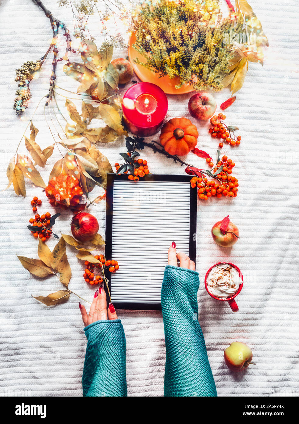 Mani femminili con lettera vuota di bordo su coltre bianca con sfondo giallo autunno rami e foglie, candele accese , zucche, rosso Coppa del cappuc Foto Stock